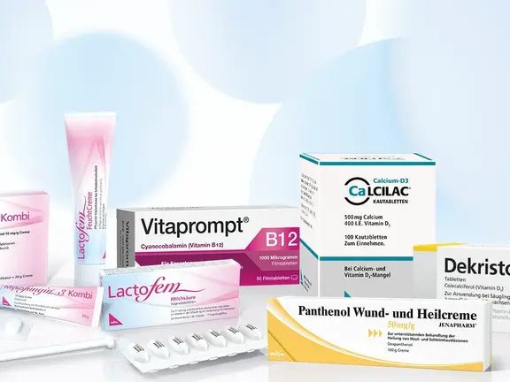 Mehrere Schachteln und Tuben mit Medikamenten mit deutschen Etiketten sind auf einer weißen Fläche mit hellblauem abstrakten Hintergrund angeordnet.